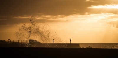 剪影照片的人类站在沙滩海岸在橙色的日落
